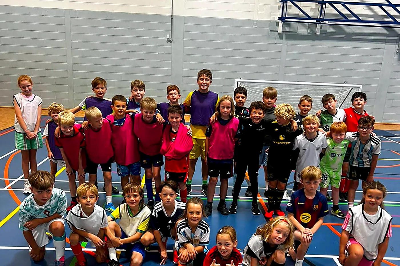 Children posing together on the sports hall floor at an indoor camp