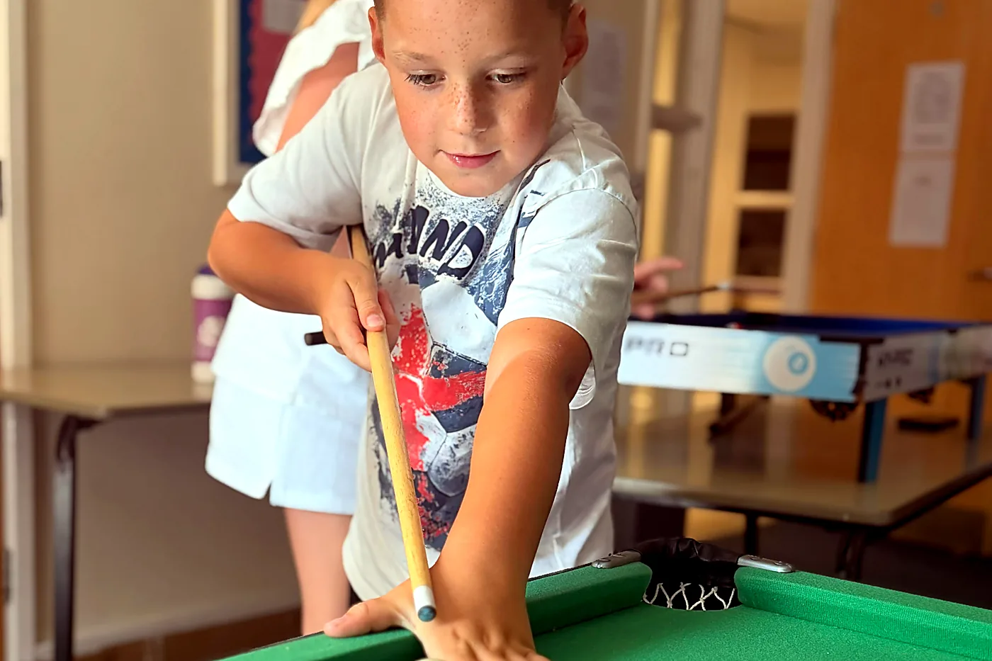 A boy playing pool during a rainy-day activity at a holiday camp