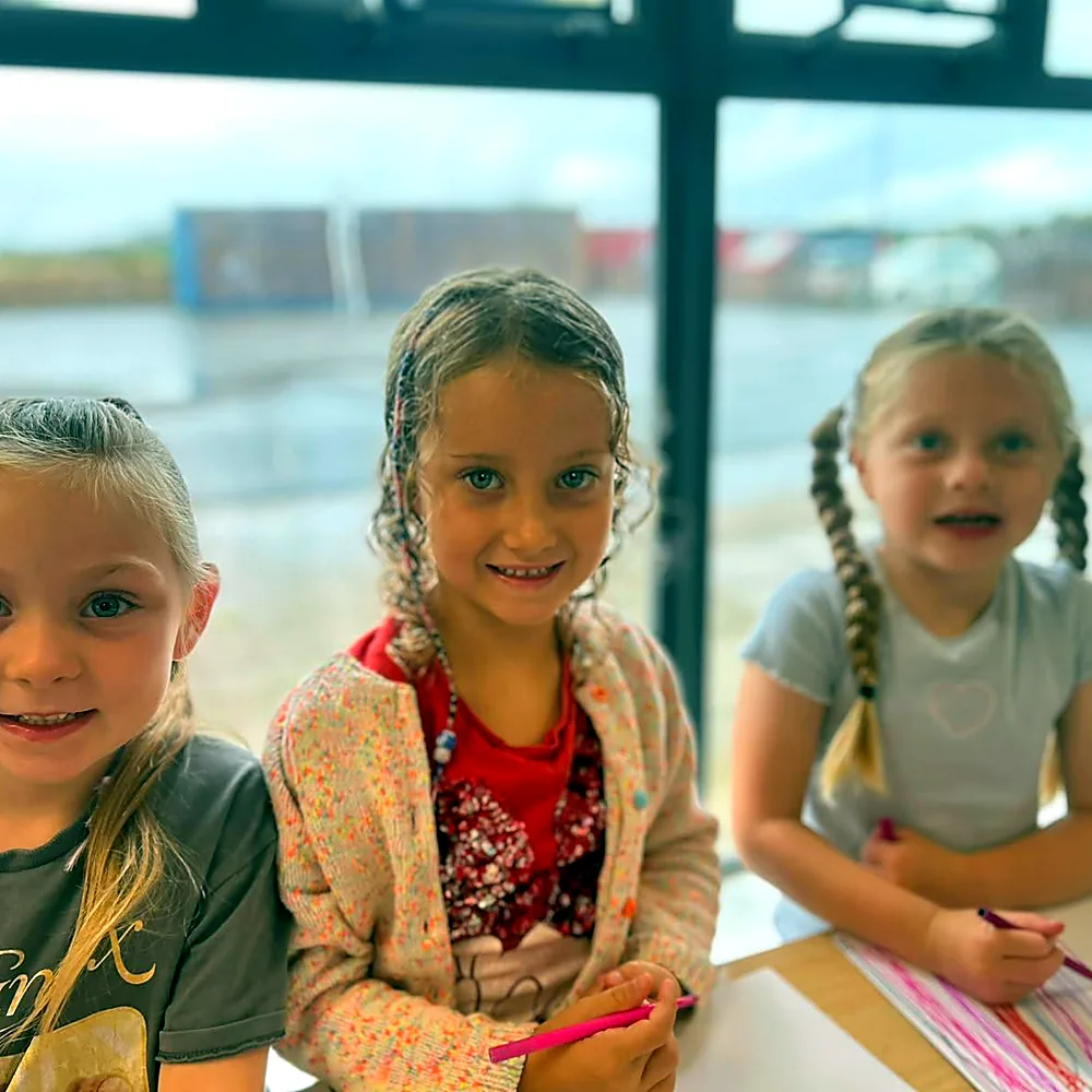 Three children colouring at a table during quiet time at a holiday camp